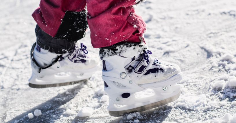Dziewczynka w białych łyżwach bawi się na lodowisku