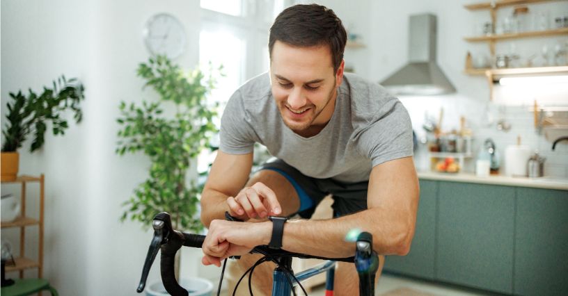 Mężczyzna trenując aeoby na rowerze treningowym sprawdza puls na smartwatchu