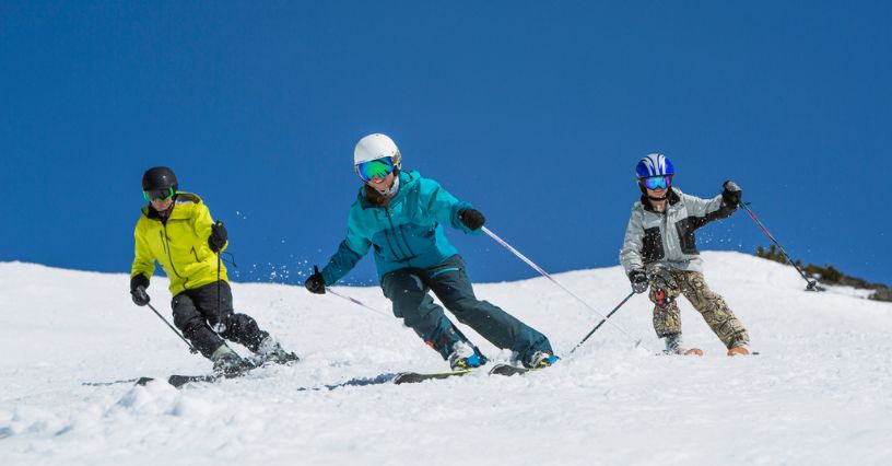 Narciarze w kolorowych kurtkach zjeżdżają razem po śnieżnym stoku