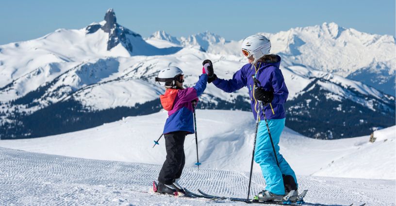 Naśnieżnym stoku kobieta i dziecko cieszą się wspólną jazdą na nartach