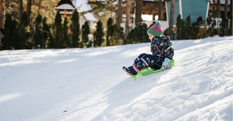 Dziecko w ciepłych śniegowcach zjeżdża na sankach z zaśnieżonej górki