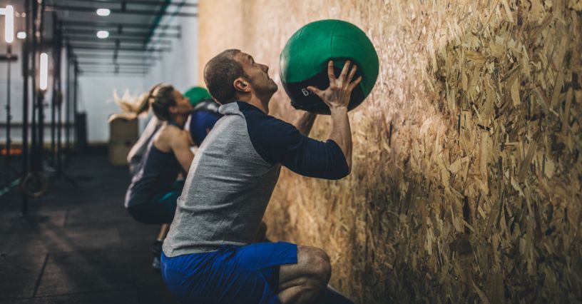 Mężczyzna w stroju sportowym trenuje wall ball na siłowni