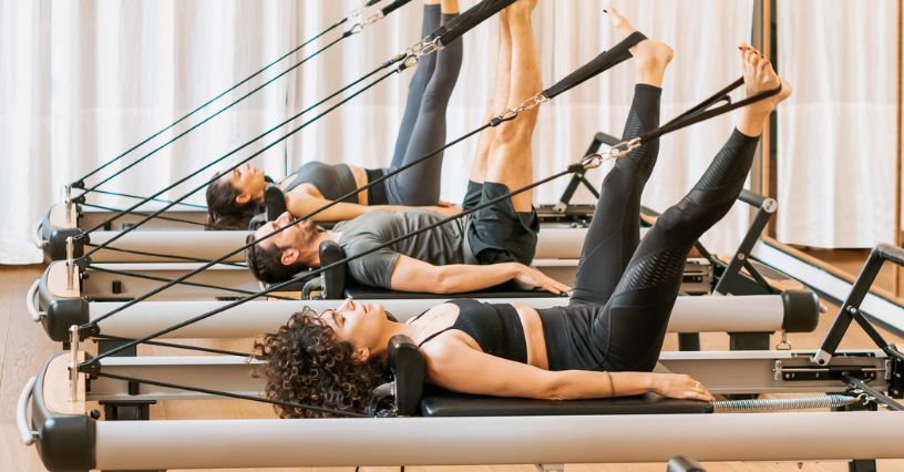 Grupa ćwiczących na reformerach w pozycji leżącej podczas zajęć pilates