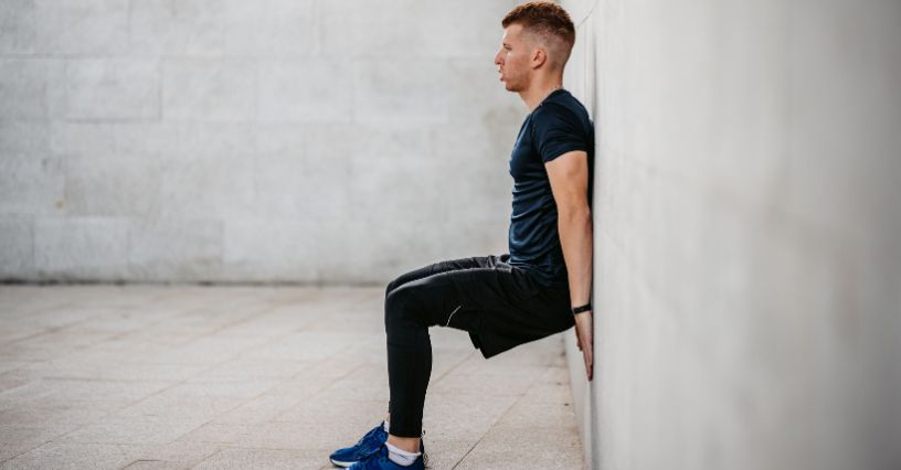 Mężczyzna wykonuje ćwiczenie krzesełko przy ścianie