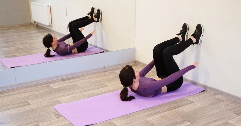 Kobieta wykonuje ćwiczenie pilates "setka" przy ścianie na macie 