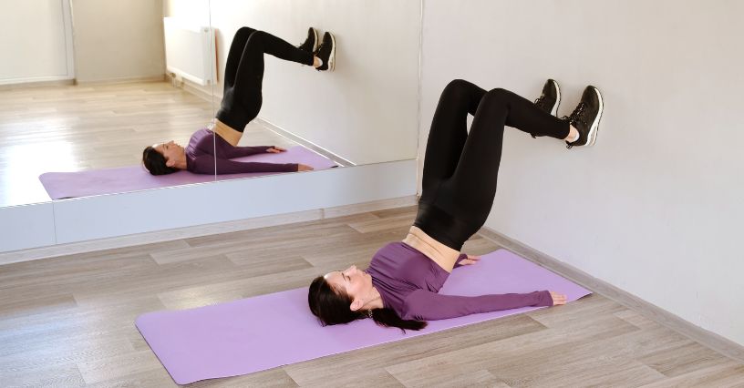 Kobieta wykonuje wznosy bioder przy ścianie na macie fitness 