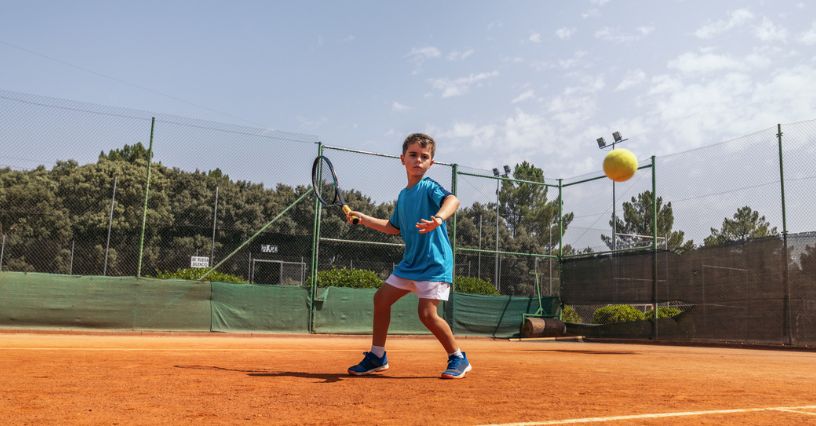 Chłopiec uczy się grać w tenisa na korcie