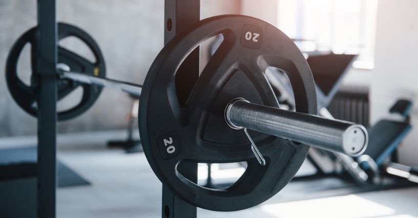 Sztanga z żeliwnymi talerzami umieszczona na stojaku w domowej siłowni