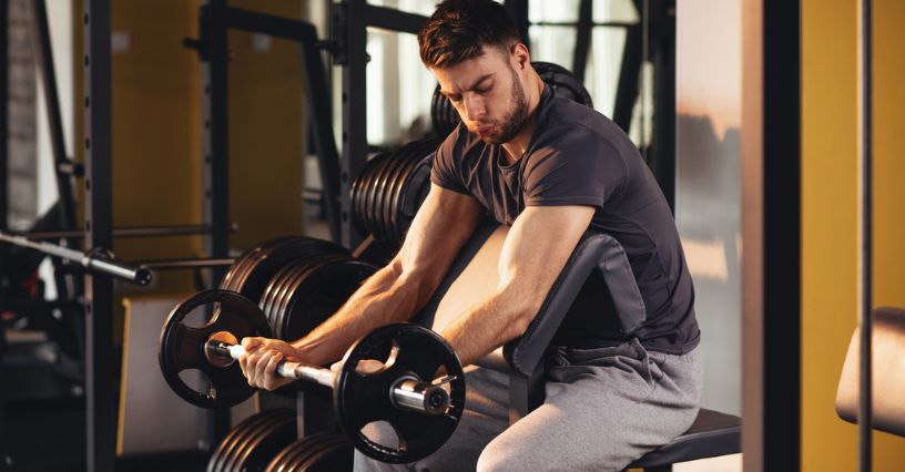 Mężczyzna ćwiczący biceps ze sztangą z żeliwnym obciążeniem