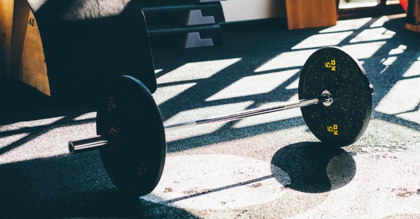 Sztanga z pełnymi talerzami leży na podłodze w domowej siłowni