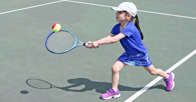 Dziewczynka na korcie tenisowym trzyma rakietę i celuje w piłkę