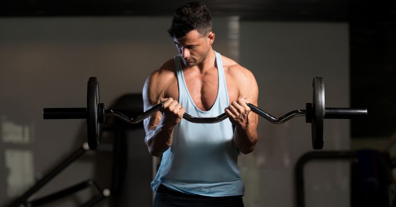 Mężczyzna ćwiczy bicepsy, używając łamanego gryfu w siłowni 
