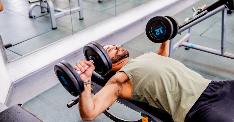 Mężczyzna wykonuje wyciskanie hantli na ławce poziomej w siłowni 