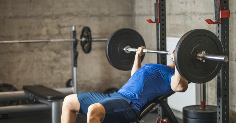 Mężczyzna wyciska sztangę na ławce dodatniej w siłowni 