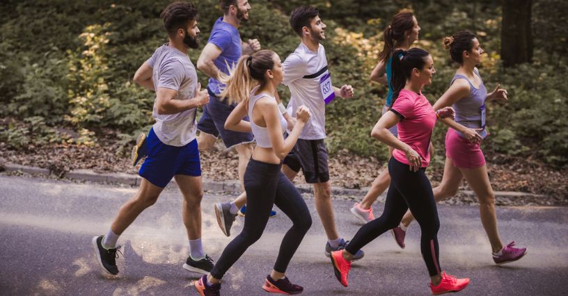 Grupa biegaczy biegnie w zawodach po asfalcie w lesie