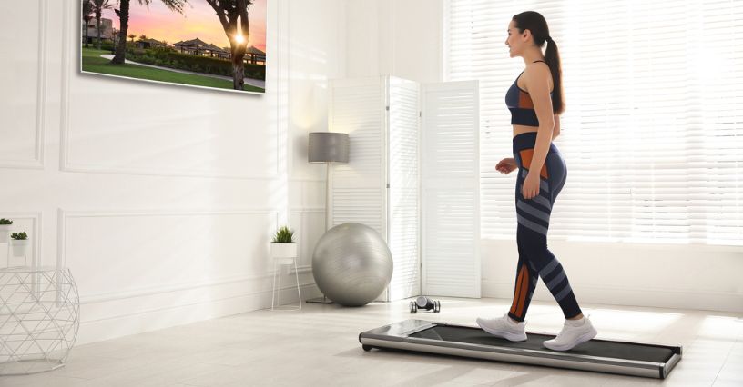 Kobieta w stroju sportowym ćwiczy na bieżni do chodzenia w domu w jasnym pokoju