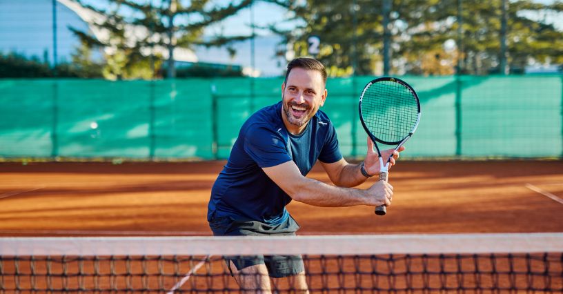 Uśmiechnięty mężczyzna w stroju sportowym gra w tenisa na korcie ziemnym
