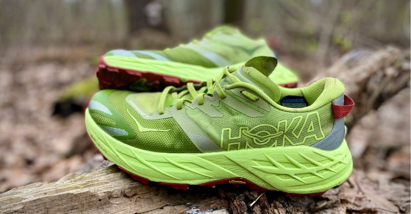 Buty trailowe HOKA Speedgoat 7 postawione na konarze drzewa wśród brązowych liści