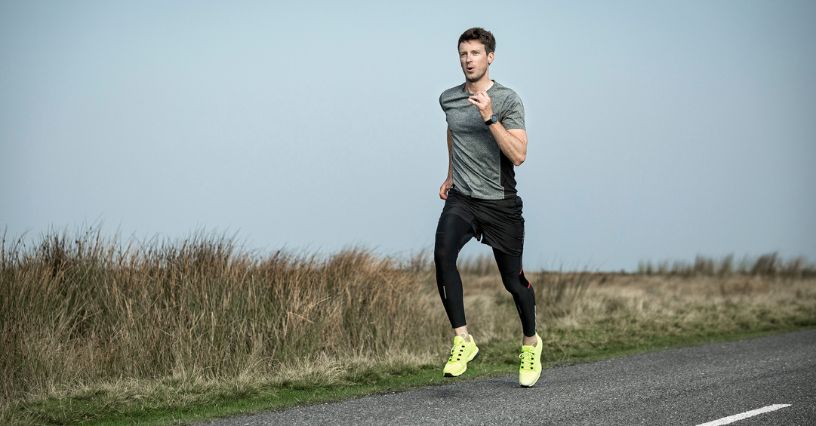 Mężczyzna w stroju sportowym biegnie asfaltową drogą