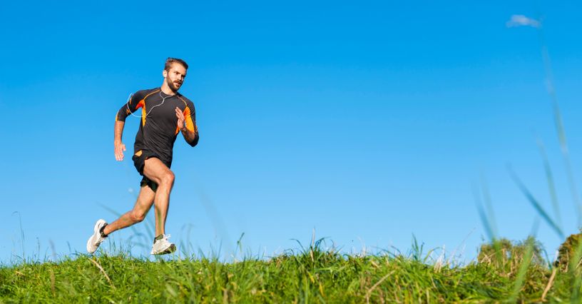 Mężczyzna w stroju sportowym szybko biegnie ścieżką wśród traw