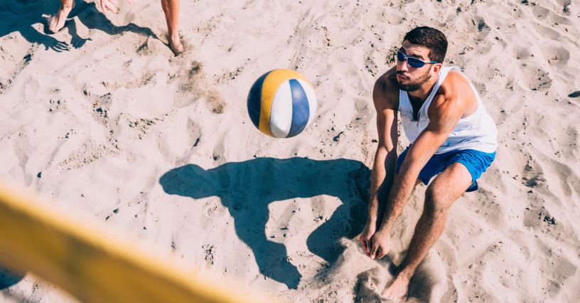 Mężczyzna w sportowych okularach przeciwsłonecznych odbija piłkę podczas gry w siatkówkę plażową