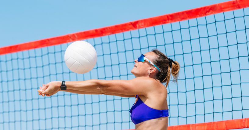 Kobieta w sportowych okularach przeciwsłonecznych odbija piłkę podczas gry w siatkówkę plażową