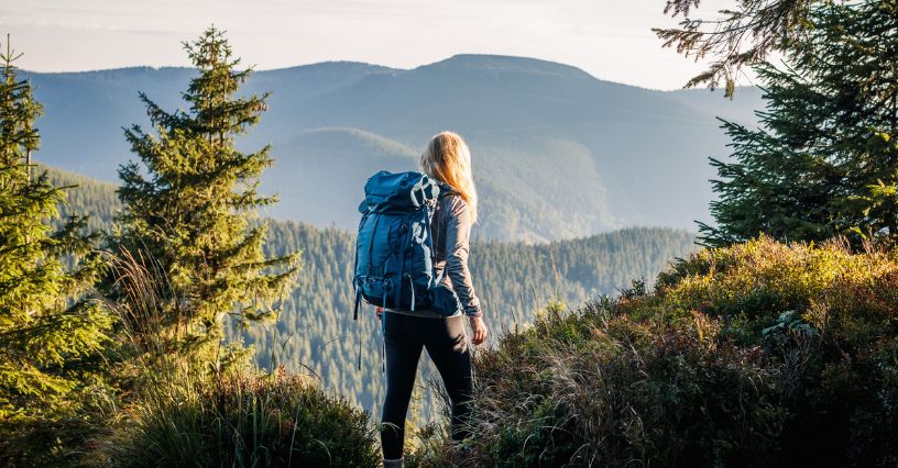 Kobieta z plecakiem trekkingowym stoi na przełęczy spoglądając na góry