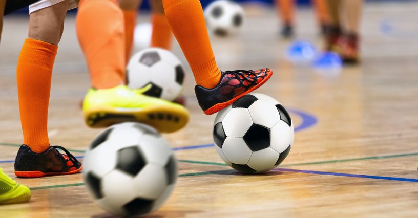 Stopy piłkarzy w butach do futsalu ustawione na piłkach położonych na parkiecie