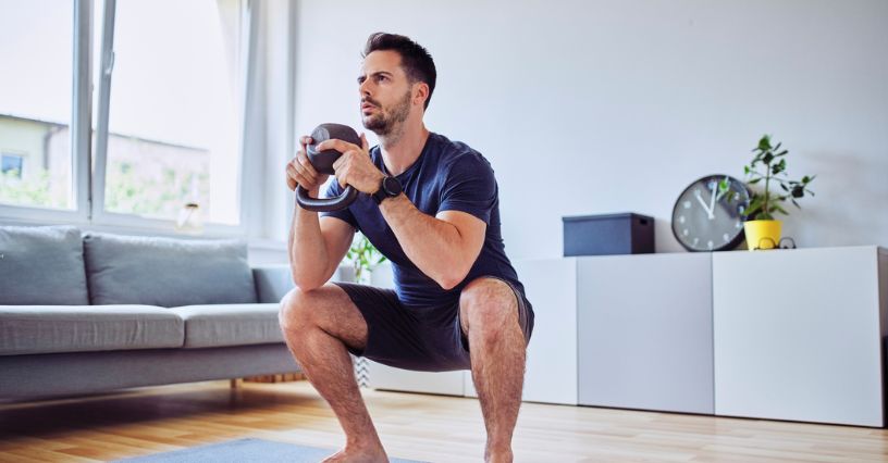 Mężczyzna robi przysiady z kettlebell na macie w domu