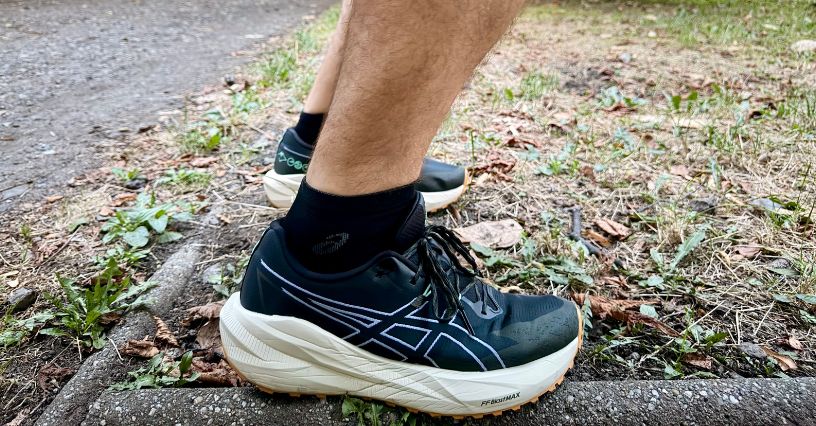 Noga biegacza w butach biegowych ASICS Blazeblast i skarpetach ASICS Performance Run Quarter na krawężniku