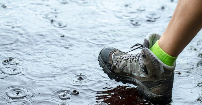 Noga turystyki w butach trekkingowych idąca po kałuży w deszczu