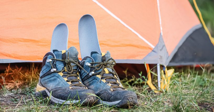 Buty trekkingowe z wyjętymi wkładkami suszą się na trawie przy namiocie 